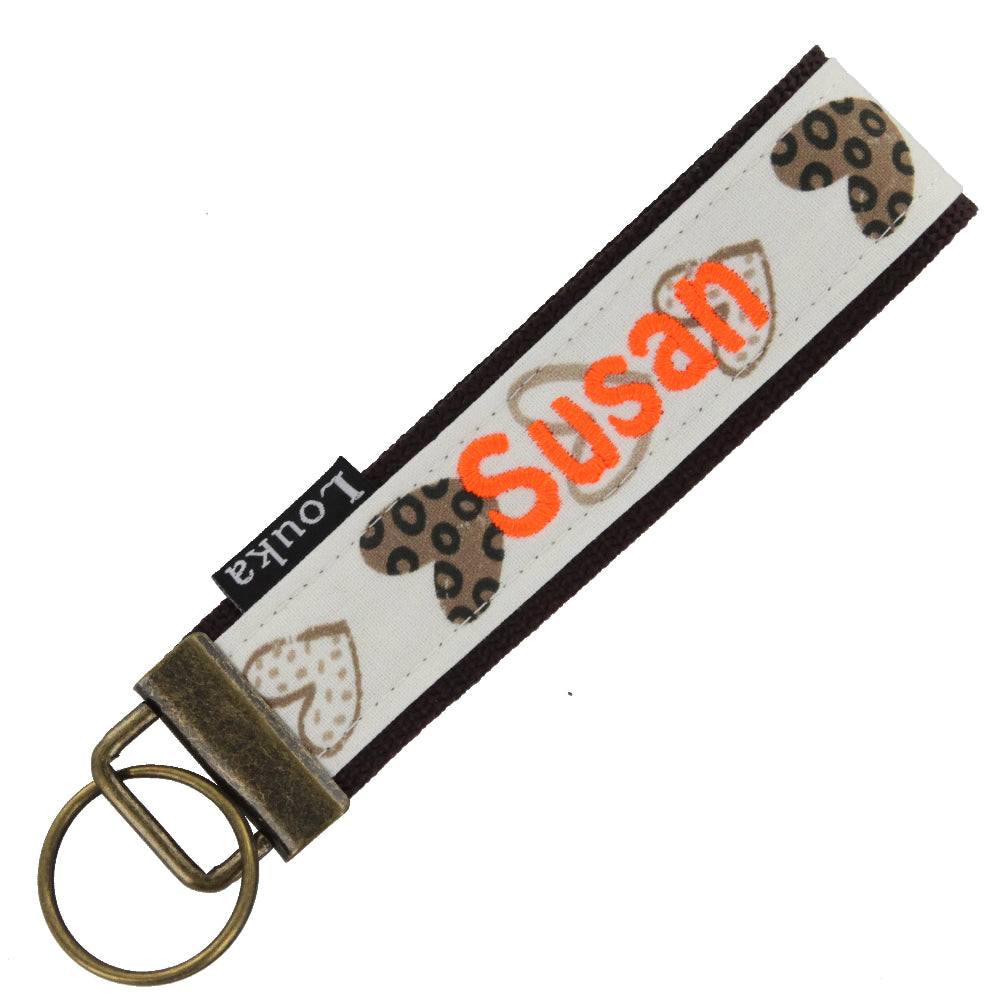 Handgemaakte Louka pols sleutelhanger met bruine hartenprint, personaliseerbaar met naam en hardware, formaat 13×3 cm.